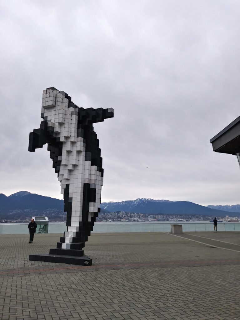 an orca whale statue in front of a body of water and mountains